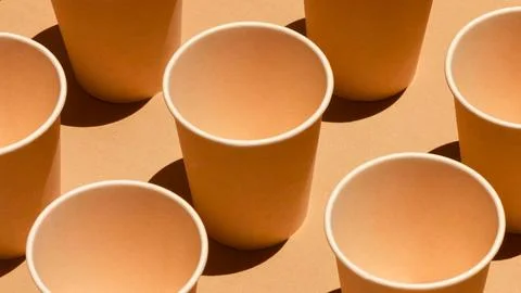Arrangement of empty orange paper cups casting shadows on a tan surface Stock Photos