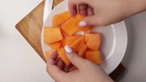 Arranging sliced orange melon pieces on white plate. Close-up of hands preparing Stock Footage 316675990