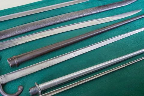 Array of antique metal swords on a dark fabric surface, varying lengths and d Stock Photos