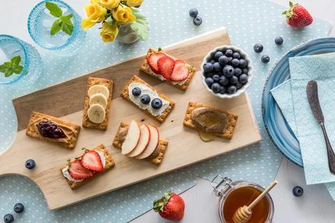 An array of breakfast crackers with a variety of toppings on a wooden board. Fotos de archivo