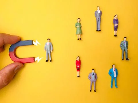 Array of figurines arranged in a pattern with a magnet and an arrow pointing in Stock Photos