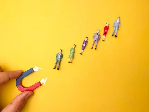 Array of figurines arranged in a pattern with a magnet and an arrow pointing in Stock Photos