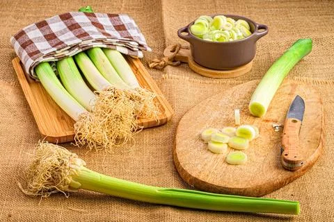Array of fresh garlic leeks arranged on a cutting board with a bowl beside them Foto stock