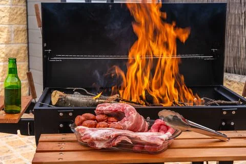 Array of raw meats and sausage near a burning grill with flames 스톡 사진