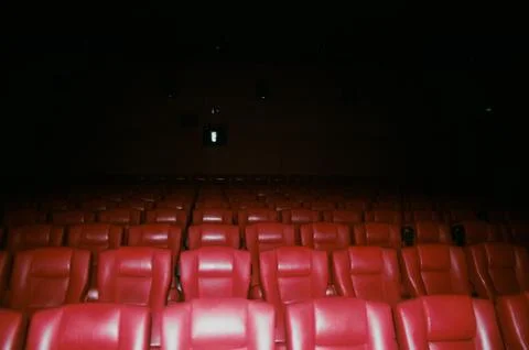 Array of red-illuminated cinema chairs in a dark room, illuminated by a warm sof Stockfoto's