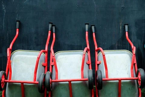 Array of red wheelbarrows lined up against a dark textured wall Stock Photos