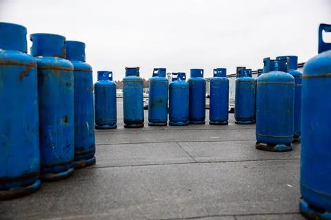 Array of used blue propane gas cylinders lined up on concrete floor, essent.. Stock Photos