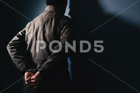 Arrested male criminal with handcuffs facing prison wall Stock Photos