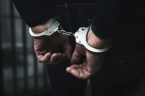 Arrested man with cuffed hands behind prison bars Stock Photos