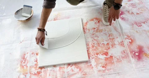 Arriving beside canvas, man is scooping compound with notched trowel and shaping Stock Footage 336174419