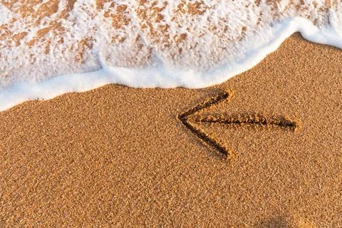 An arrow drawn on the sand pointing to the left next to sea foam An arrow ... Foto stock