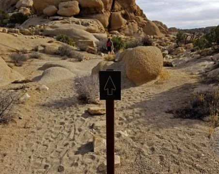 Arrow pointing to path on desert trail with hiker in the distance Stock Photos