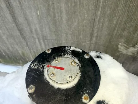 Arrow Points to Open Indicator on a Black Valve Covered in Snow Near a Grey.. Stock Photos
