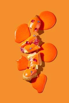 Art with an eclair. Broken eclair in puddles of icing on an orange backgrou.. Foto stock