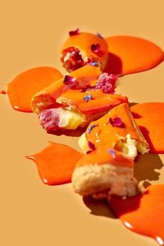 Art with an eclair. Broken eclair in puddles of icing on an orange backgrou.. Stock Photos