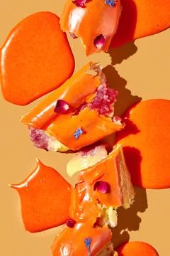 Art with an eclair. Broken eclair in puddles of icing on an orange backgrou.. Stock Photos