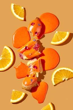 Art with an eclair. Broken eclair in puddles of icing on an orange backgrou.. Stock Photos