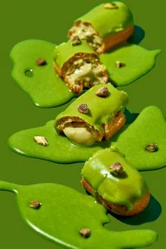 Art with an eclair. Broken eclair in puddles of icing on green background. .. Stock Photos