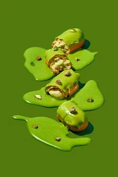 Art with an eclair. Broken eclair in puddles of icing on green background. .. Stock Photos