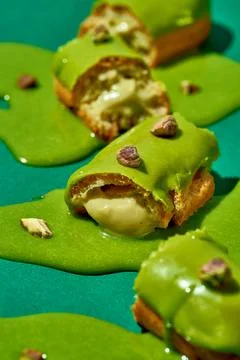 Art with an eclair. Broken eclair in puddles of icing on green background. .. Stock Photos