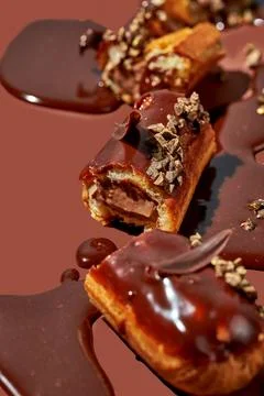 Art with an eclair. Broken eclair in puddles of icing on brown background. .. Stock Photos