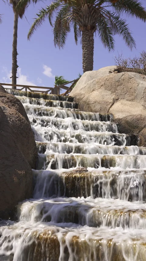 An artificial fountain descending down steps against a backdrop of palm trees Stock Footage 285772263