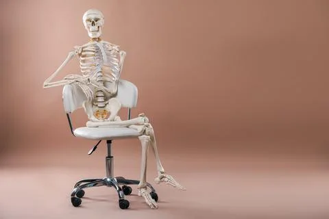 Artificial human skeleton model sitting on chair against light brown backgr.. Stock Photos