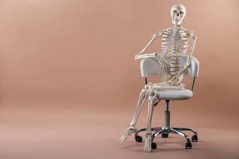 Artificial human skeleton model sitting on chair against light brown backgr.. Stock Photos