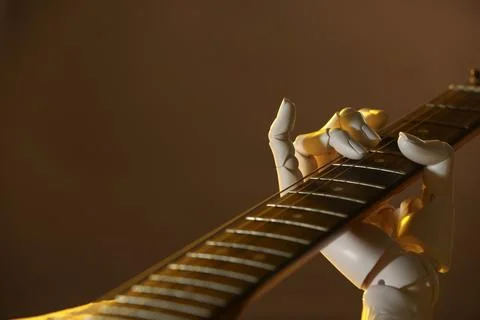Artificial intelligence. Robot hand playing guitar on brown background, close Stock Photos