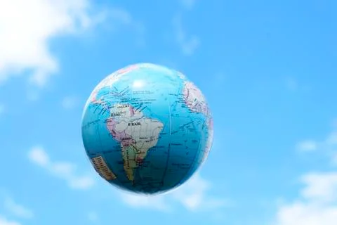 Artificial plastic globe of planet earth floating in a blue sky with clouds a Stock Photos