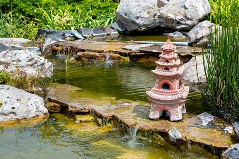 Artificial pond with the flow of waterfall and a stone sculpture. Stock Photos