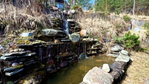 Artificial tiered stone waterfall flowing into a tranquil pond in a backyard Stock Footage 334691515