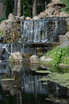 Artificial tiered waterfall cascade made of rocks flowing into a park pond Stock Photos
