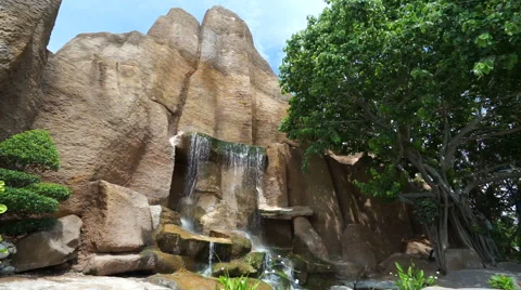 Artificial waterfall which is falling down from huge rock in a park at summer Stock Footage 67814494