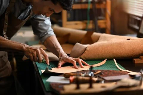 An artisan carefully using a sharp knife to shape the leather on cutting mat in Stock Photos