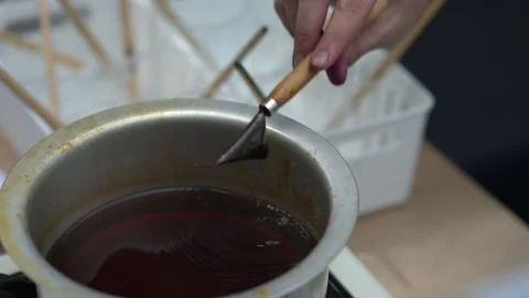 Artisan dipping a canting tool into a pot of melted wax for batik craft Stock Footage 346349416