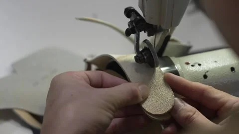 Artisan feeding a rolled suede strip through a sewing machine to bind a glove Stock Footage 340276659