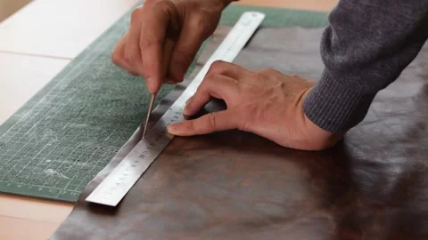 Artisan making markings on a sheet of brown leather with a ruler and awl. Stock Footage 150477682