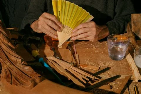An artisan meticulously creating a decorative folding fan using various woode Stock Photos