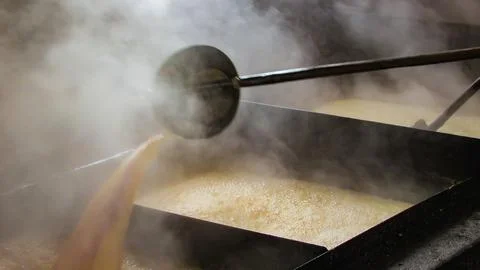 Artisan process of boiling raw sugarcane juice in large open pans to create.. Stock Photos