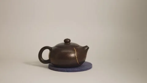 An artisan tea pot with a gold kintsugi repaired crack rotates on a white Stock Footage 289176922
