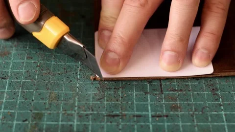 Artisan uses a knife to round the corners of the leather cardholder. Stock Footage 150480347