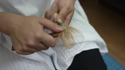 Artisan weaving thread between the tines of a bamboo tea whisk on her lap Stock Footage 348098587