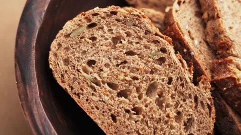 Artisanal dark grain bread slice falling into a wooden bowl Stock Footage 333621839