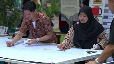 Artisans applying hot wax with canting tools on white fabric during a batik Stock Footage 346350303