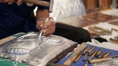 Artisan's hands are embossing a silver sheet using a hammer and punch Stock Footage 345128293
