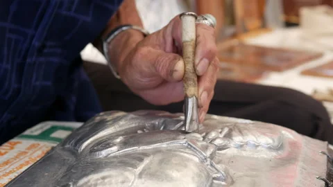 Artisan's hands are embossing a silver sheet using a hammer and punch Stock Footage 345128574