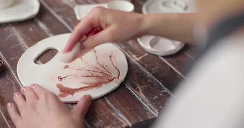 Artist creates a beautiful pattern on earthenware in a pottery workshop. Close Stock Footage 155555348
