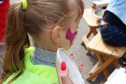Artist face painting a blond haired girl with a brush. Stock Photos