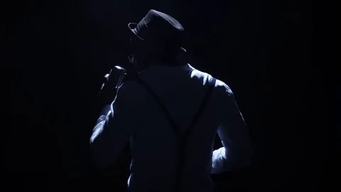 Artist in the hat a weak light at the microphone singing the song. Black Stock Footage